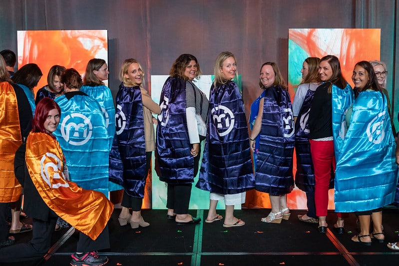 M&IW team members standing on stage wearing superhero capes with the M&IW logo on them