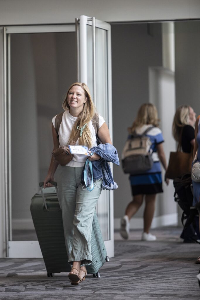 Event attendee walking down a hallway holding a name badge and pulling a suitcase