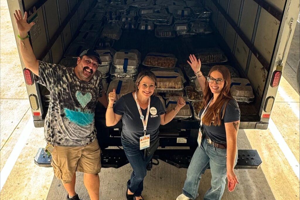 Event staff smile in front of a truck bed of food being donated