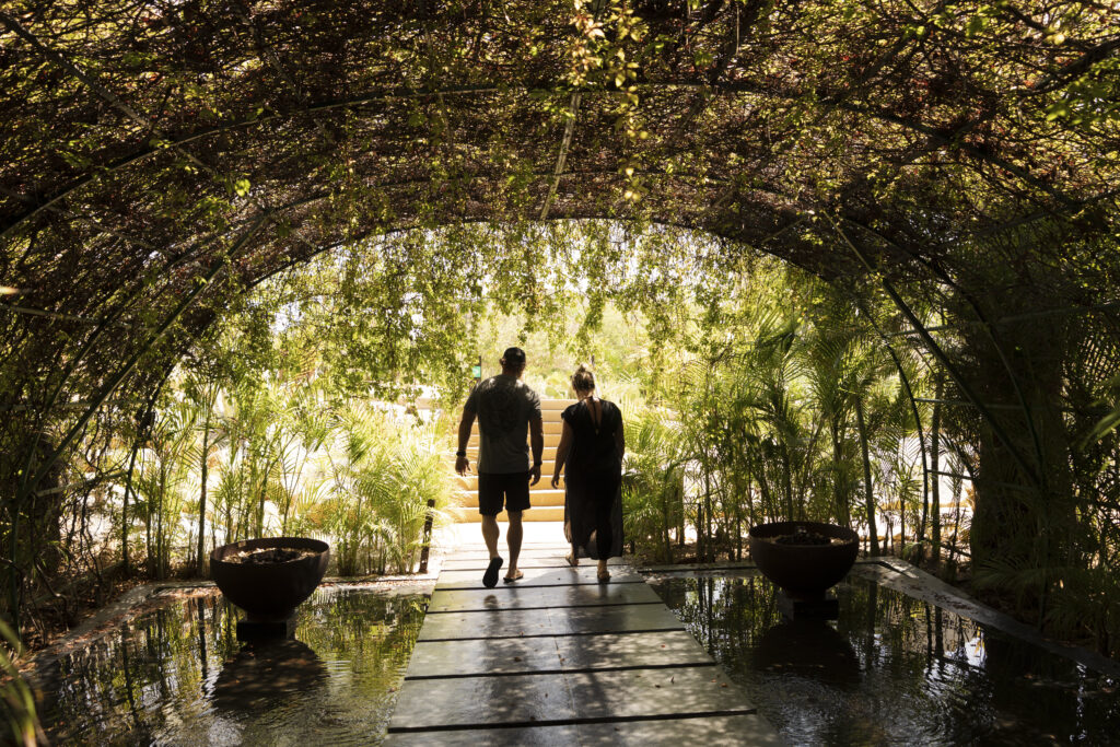 A man and woman walk under an arch of greenery